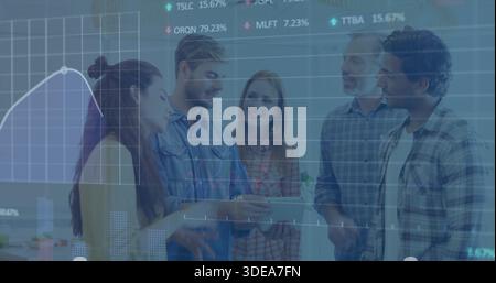 Reviewing group of five in casual shirts, leaning around tablet in office, showing finance charts Stock Photo