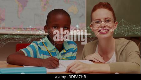 Writing boy striped-polo holding pencil over spiral-notebook at school desk, tutor leaning glasses Stock Photo