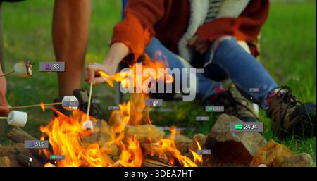 Roasting couple in rust jacket and hiking boots, holding marshmallows over campfire, with badges Stock Photo