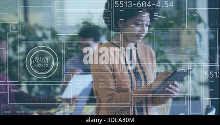 Holding tablet, focused woman in rust-brown cardigan analyzing data with HUD overlays in office Stock Photo