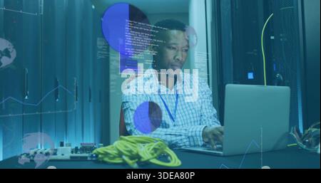 Working tech typing laptop in server room aisle, wearing checked shirt, blue lanyard, yellow cables Stock Photo