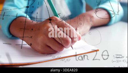 Writing right-hand with green pencil doing math in ruled book orange edge at desk, turquoise sleeve Stock Photo