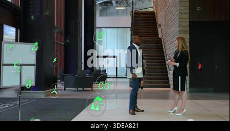 Talking colleagues wearing navy suit and black blazer in lobby, holding laptop, coffee, AR overlays Stock Photo