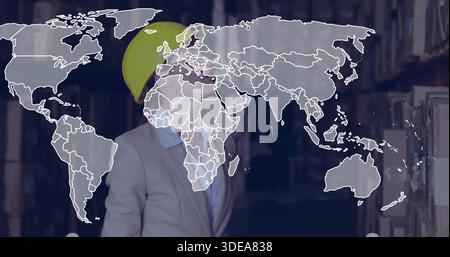 Standing woman in yellow hard hat, light blazer inspecting warehouse racks with world map overlay Stock Photo