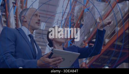 Inspecting two managers in suits reviewing stock in warehouse near pallet racking, holding tablet Stock Photo