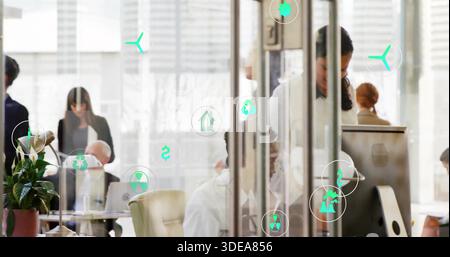 Working team in suits using computers in open-plan office by glass walls, displaying green icons Stock Photo