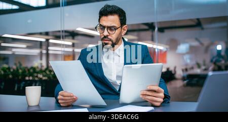 Businessman Reads Reports and Checks Tablet in Modern Office Setting During Work Hours Stock Photo