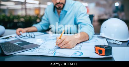 Engineer Works on Building Design Plans at a Construction Project Site During the Day Stock Photo