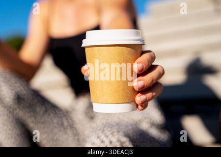 Close-up of paper coffee cup in female hand outdoors. Stock Photo