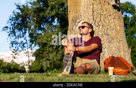Relaxed man sitting on grass in the park enjoying urban nature. Stock Photo
