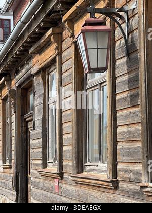 Weathered wooden building with decorative windows and vintage lantern mounted on facade Stock Photo