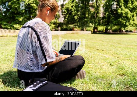 E-learning and digital education. Young urban woman studying remotely in public park using her laptop. Stock Photo