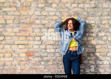 Casual lifestyle. Young female wearing denim outfit posing near brick wall in city. Stock Photo