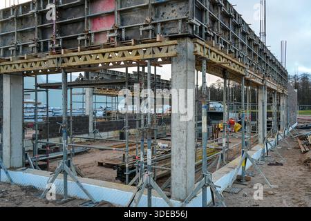 Construction site showing concrete formwork, columns, supports, scaffolding, and workers preparing structural foundations for a commercial building Stock Photo