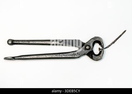 Old blacksmith pincers gripping a rusty nail, isolated on white background. Vintage hand-forged metal tool showing wear, history and craftsmanship Stock Photo