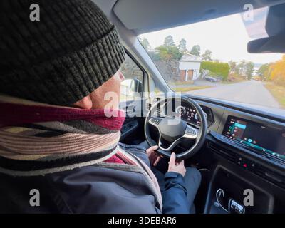 Calm strength senior lifestyle with an older man driving a modern car from rear seat view in daylight, hands on steering wheel, winter clothing, quiet Stock Photo