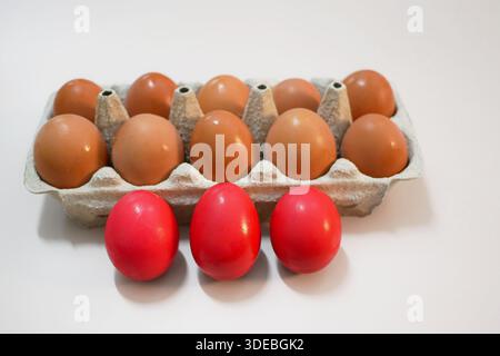 Red dyed Easter eggs placed in front of a carton of natural brown eggs. Festive spring composition for Easter, tradition, and holiday themes. Stock Photo