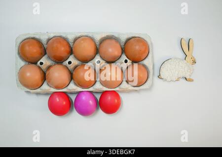 Red dyed Easter eggs placed in front of a carton of natural brown eggs. Festive spring composition for Easter, tradition, and holiday themes. Stock Photo