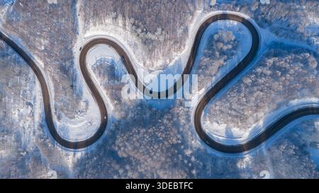 A dramatic aerial shot of a sharp-curved mountain road illuminated by sunlight reflecting off snowflakes. The dance of light and shadow over the winte Stock Photo