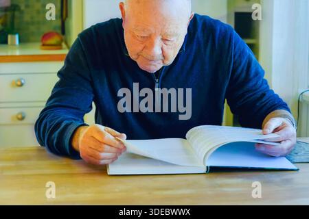 Mindful focus on everyday learning and mature lifestyle with an older man reading book at wooden table indoors, concentrated posture and quiet environ Stock Photo