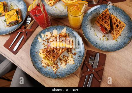 Waffles served with toppings are placed alongside colorful juices in glasses. The dishes are arranged on blue plates atop a wooden table, creating an Stock Photo