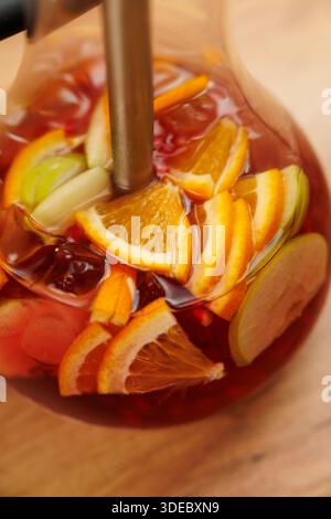 Fruit punch made with orange, lemon, and lime slices mixed with berries is poured from a glass pitcher at a summer gathering. The bright colors attrac Stock Photo