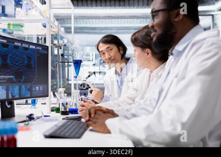 Multiethnic lab researchers team evaluating genetic markers associated with disease risk on PC. Multiracial laboratory engineers study DNA strand mapping with genomics analysis program on computer Stock Photo