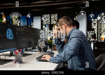 Tired man drinks coffee while utilizing AI on computer to optimize performance. Exhausted worker enjoys caffeinated beverage in tech company office while training deep learning models Stock Photo