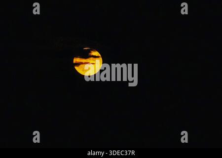 Travel romania transilvania targu mures bright yellow full moon partially hidden by dark clouds in black night sky Stock Photo