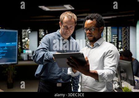 Team of programmers in office doing brainstorming, automating repetitive tasks using AI scripts on devices. Colleagues work together using artificial intelligence to speed up feature implementation Stock Photo