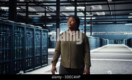 Portrait of cheerful data center engineer conducting security audits to protect against cyber threats. Jolly worker walking in server room, ensuring compliance with industry standards, camera A Stock Photo