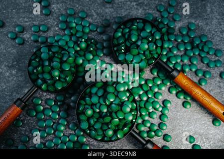 Spirulina tablets fall into measuring cups with wooden handles. Top view.Algae in nutrition.Natural vegetarian source of protein. Stock Photo