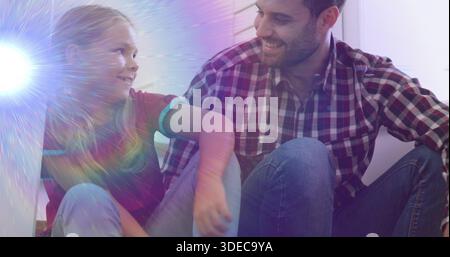 Smiling child beside adult man sitting on floor in hallway, showing plaid shirt, jeans, lens flare Stock Photo