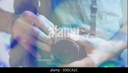 Holding man in T-shirt handling manual SLR camera at chest in studio, showing strap and wristband Stock Photo