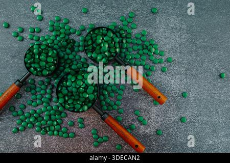 Spirulina Pills with Measuring Spoons on Dark Background. Algae superfood.Supplements for health and longevity. Natural source of iodine. Super food. Stock Photo