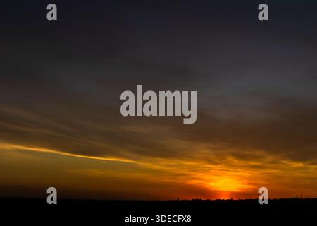 A dramatic sunset paints the sky with fiery orange and golden hues over a silhouetted landscape. The last light of day creates a serene and beautiful Stock Photo