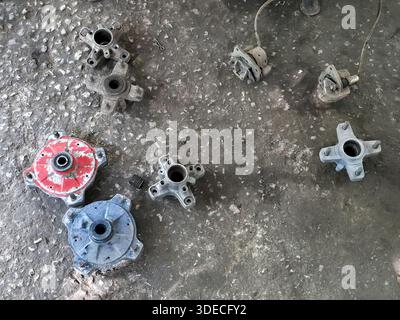 Scattered old rusty car parts mechanical gears and metal components lying messy on dirty concrete floor in garage workshop with greasy texture Stock Photo