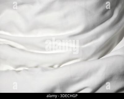 Soft wrinkled white bed sheet fabric texture background looking gentle pure and calm showing smooth abstract pattern of textile surface detail in ligh Stock Photo