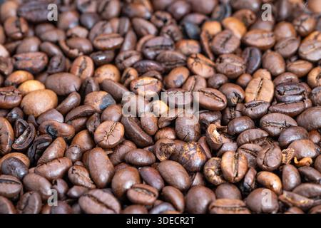 Macro dense roasted coffee beans arranged in uniform pile, deep dark tones and subtle sheen, ideal for wholesale packaging, supply catalogs and backgr Stock Photo