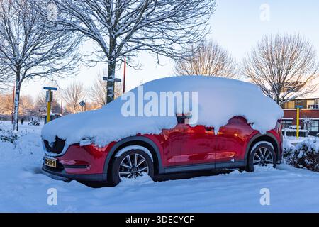 Red SUV car parked in a residential street completely covered with a thick layer of white snow during a freezing cold winter day in the Netherlands. U Stock Photo