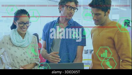 Analyzing three team members in casual attire leaning over laptop at open office, showing AR icons Stock Photo
