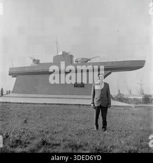 Izmail, Odessa region, Ukrainian SSR, Soviet Union, 1975. A male tourist posing for a souvenir photo in front of the famous Monument to the Armored Motor Gunboat BK-134 near the Danube Commercial Port. The black and white archive image shows a man in a suit standing on the grass, with industrial cranes visible in the distance. The memorial is dedicated to the Danube Flotilla sailors who liberated the city. The shot captures the atmosphere of patriotic tourism and peaceful leisure in the southern city during the stable USSR era. Stock Photo