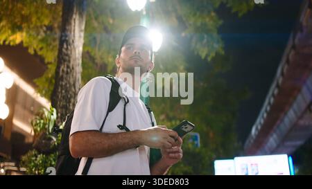 Young male traveler navigating city street at night using smartphone in bangkok Stock Photo