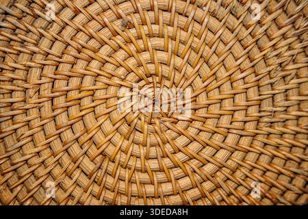 Close-up of a circular woven rattan texture with a spiral pattern, natural brown fiber background for design. Stock Photo
