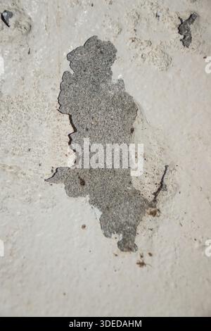 Close-up of peeling off-white paint revealing a grey concrete surface. Weathered wall texture for abstract background and urban design. Stock Photo