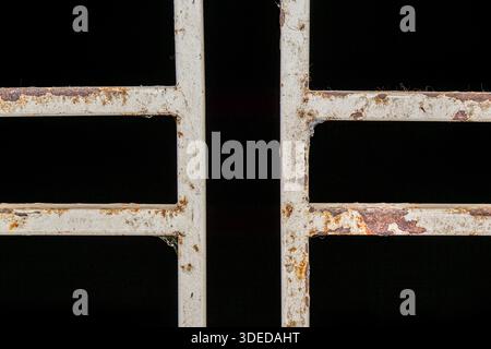 Close-up of a rusty white metal gate against a black background, showing industrial decay and weathered texture. Stock Photo