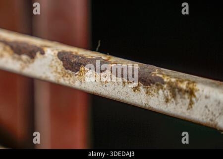 Close-up of a rusty metal bar with peeling white paint and deep corrosion against a dark background, showing signs of industrial decay. Stock Photo