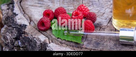 Raspberry essential oil in a bottle with fresh berries on a wooden stump Stock Photo