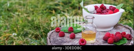 Raspberry essential oil in a bottle with fresh berries on a wooden stump Stock Photo