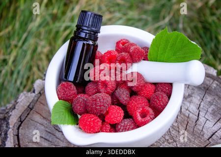 Raspberry essential oil in a bottle with fresh berries on a wooden stump Stock Photo